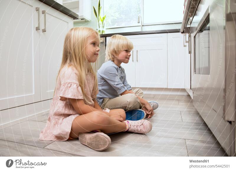 Bruder und Schwester sitzen in der Küche auf dem Boden und schauen auf den Ofen Junge Buben Knabe Jungen Knaben männlich sitzend sitzt Schwestern ansehen