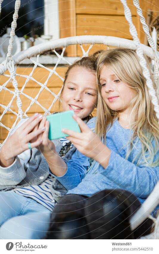Porträt von zwei Mädchen, die sich in einem Hängesessel entspannen und ein Selfie mit ihrem Smartphone machen Haengesessel iPhone Smartphones Selfies Portrait