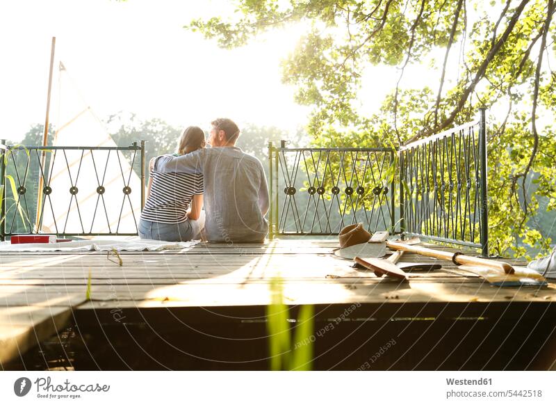 Junges Paar sitzt auf einem Steg neben einem Segelboot sitzen sitzend Pärchen Paare Partnerschaft Stege Anlegestelle Segelboote Segelschiff Mensch Menschen
