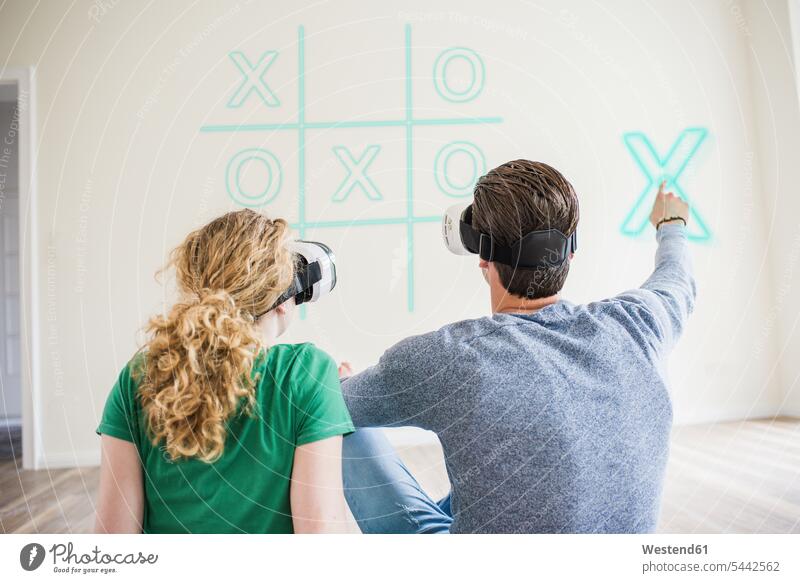 Junges Paar mit VR-Brille spielt virtuellen Tic-Tac-Toe Virtualität spielen Pärchen Paare Partnerschaft Wohnung wohnen Wohnungen Mensch Menschen Leute People