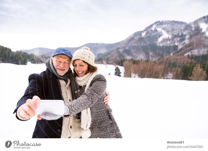 Älteres Paar, das sich küsst und ein Selfie mit dem Handy in einer Winterlandschaft macht Seniorenpaar älteres Paar Seniorenpaare ältere Paare Seniorenpärchen