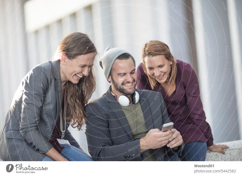 Drei fröhliche junge Leute schauen gemeinsam aufs Handy Kollegen Arbeitskollegen Mobiltelefon Handies Handys Mobiltelefone lachen Telefon telefonieren