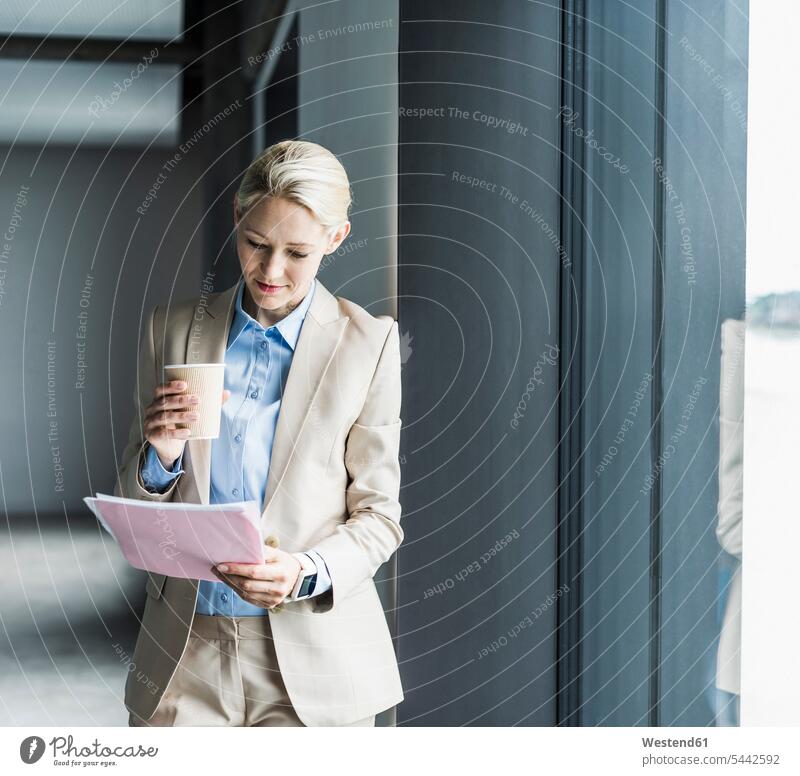 Geschäftsfrau mit Kaffee lesendem Dokument am Fenster Geschäftsfrauen Businesswomen Businessfrauen Businesswoman stehen stehend steht Lektüre Geschäftsleute