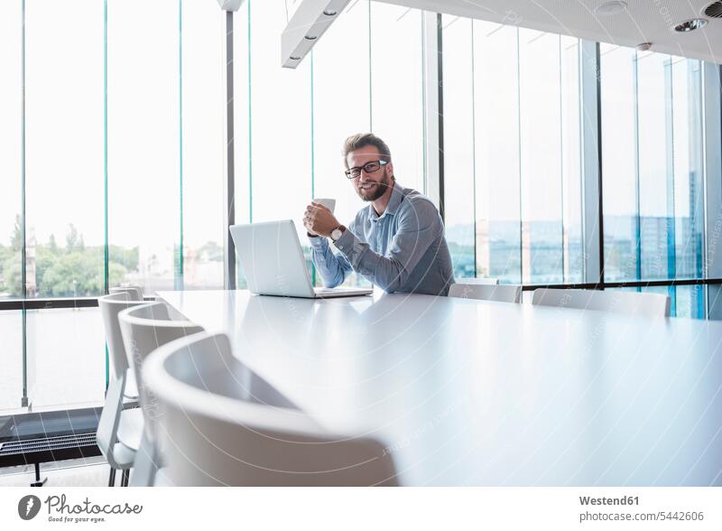 Mann mit Laptop und Tasse Kaffee sitzt am Konferenztisch im Büro Männer männlich Notebook Laptops Notebooks sitzen sitzend Geschäftsmann Businessmann