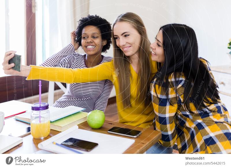 Gruppe von Studentinnen, die ein Selfie am Tisch zu Hause machen Selfies lächeln Hochschülerin Hochschülerinnen Hochschuelerinnen Tische Handy Mobiltelefon