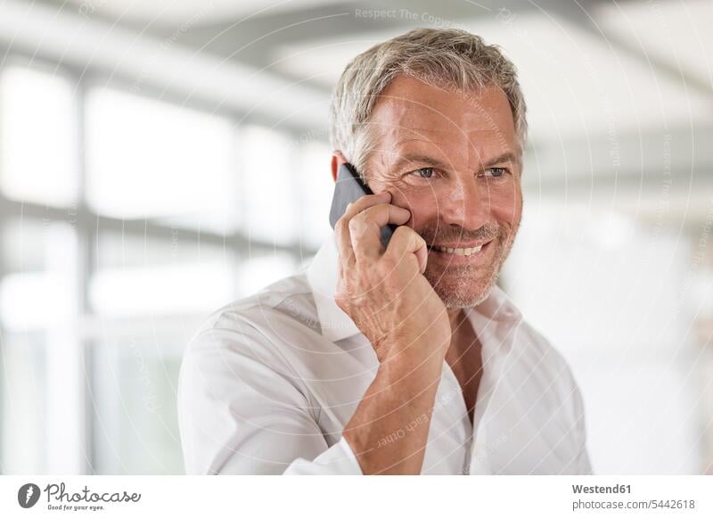 Lächelnder Geschäftsmann am Handy im Büro Businessmann Businessmänner Geschäftsmänner lächeln telefonieren anrufen Anruf telephonieren Mobiltelefon Handies