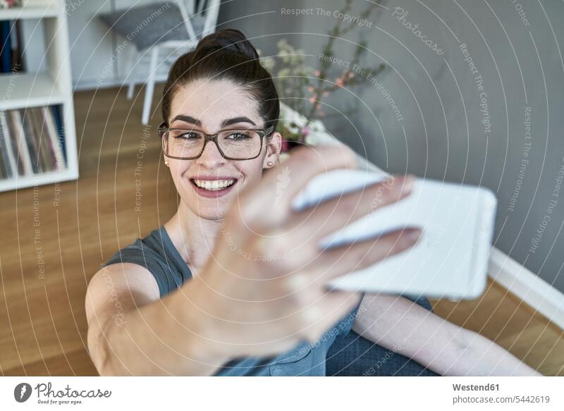 Lächelnde junge Frau macht ein Selfie zu Hause Handy Mobiltelefon Handies Handys Mobiltelefone Selfies weiblich Frauen lächeln Telefon telefonieren