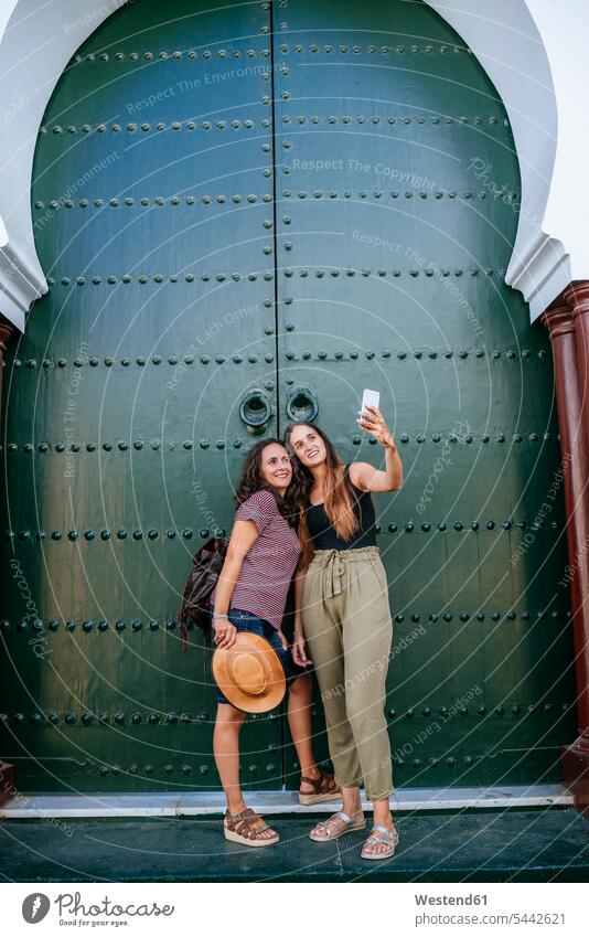 Marokko, Chefchaouen, zwei Frauen machen ein Selfie mit Smartphone vor einem grünen Portal Selfies Portale Pforten weiblich iPhone Smartphones Farbe Farbtöne