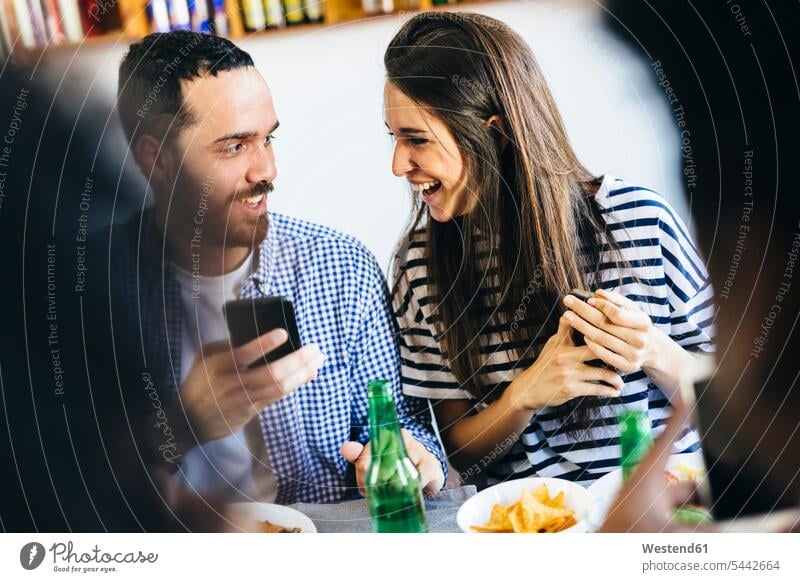 Glückliches Paar teilt sich ein Handy am Esstisch Mobiltelefon Handies Handys Mobiltelefone Tisch Tische Pärchen Paare Partnerschaft essen essend Telefon