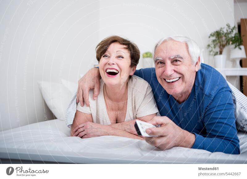 Älteres Ehepaar im Bett liegend mit Fernbedienung Europäer Kaukasier Europäisch kaukasisch Unbeschwert Sorglos Betten Beziehung lächeln Zusammengehörigkeit