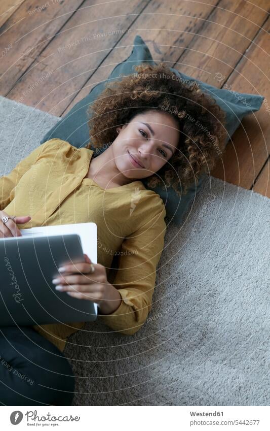 Lächelnde junge Frau liegt zu Hause mit Laptop auf dem Boden Notebook Laptops Notebooks Böden Boeden weiblich Frauen liegen liegend Zuhause daheim lächeln
