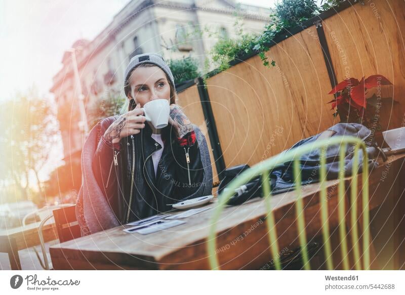 Junge tätowierte Frau sitzt in Straßencafé und trinkt Kaffee Straßencafe Straßencafes Strassencafe Strassencafes weiblich Frauen Cafe Kaffeehaus Bistro Cafes