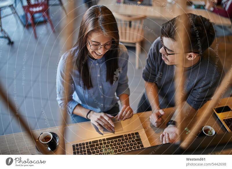 Junger Mann schaut lächelnde Frau in einem Café mit Laptop an Notebook Laptops Notebooks weiblich Frauen Cafe Kaffeehaus Bistro Cafes Cafés Kaffeehäuser Männer