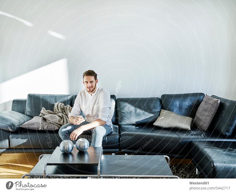 Lächelnder Mann sitzt auf der Couch und hält ein Handy lächeln Sofa Couches Liege Sofas Mobiltelefon Handies Handys Mobiltelefone sitzen sitzend Männer männlich