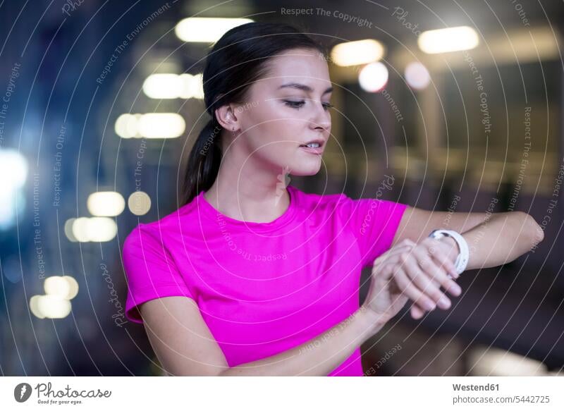 Junge Frau in rosa Sporthemd, die ihre Smartwatch kontrolliert checken junge Frau junge Frauen Uhrzeit Joggerin Joggerinnen trainieren weiblich Erwachsener