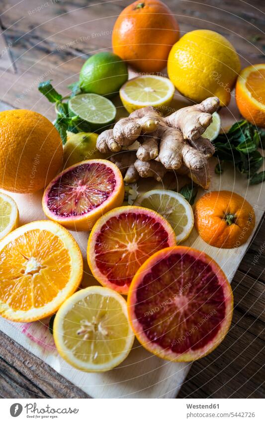In Scheiben geschnittene und ganze Zitronen, Orangen und Limetten, Ingwerwurzel und Minzeblätter auf Holzbrett Küchengewürz Gewuerz Gewürz Gewuerze