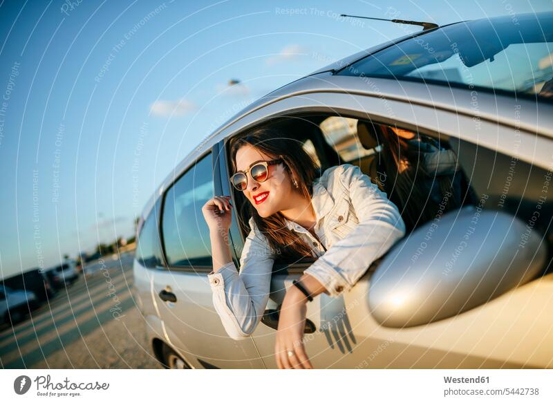 Junge Frau lehnt sich aus dem Autofenster Wagen PKWs Automobil Autos weiblich Frauen Kraftfahrzeug Verkehrsmittel KFZ Erwachsener erwachsen Mensch Menschen