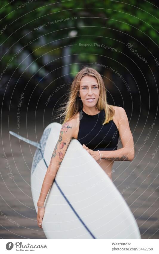 Porträt einer lächelnden Frau mit Surfbrett am Strand weiblich Frauen Surfen Surfing Wellenreiten tragen transportieren Surfbretter surfboard surfboards