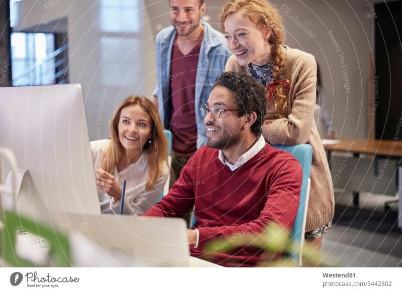 Kollegen schauen einem jungen Mann über die Schulter, der in einem modernen Büro arbeitet Team Kollegin Kolleginnen ansehen zuschauen Office Büros lächeln