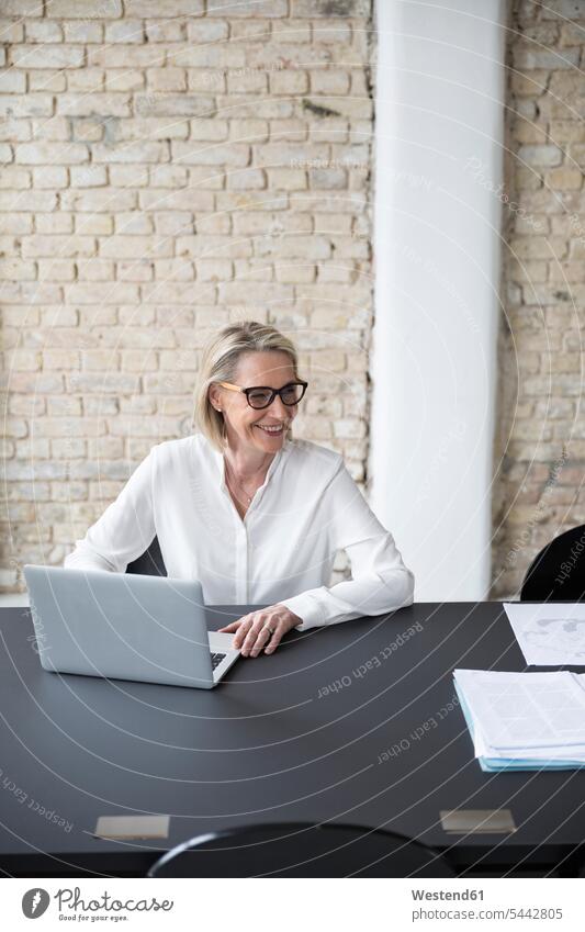 Reife Geschäftsfrau, die im Büro arbeitet und einen Laptop benutzt Schreibtisch arbeiten sitzen reife Frau Geschäftsleute Business Tisch Arbeitsplatz Computer