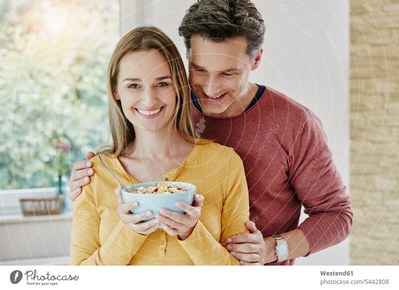 Glückliches Paar hält Schüssel mit Müsli zu Hause glücklich glücklich sein glücklichsein Portrait Porträts Portraits Muesli essen essend Pärchen Paare