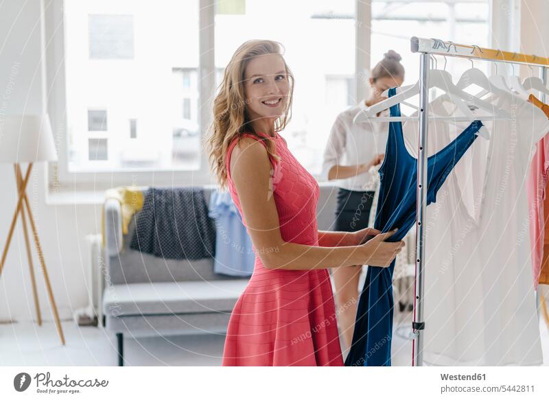 Lächelnde junge Frau wählt Kleid aus Kleiderstange weiblich Frauen Studio Atelier Studios Ateliers Mode modisch Fashion Erwachsener erwachsen Mensch Menschen