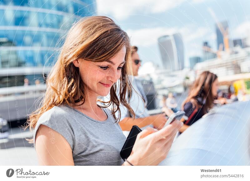 UK, London, lächelnde Frau, die ihr Smartphone kontrolliert weiblich Frauen Handy Mobiltelefon Handies Handys Mobiltelefone Erwachsener erwachsen Mensch