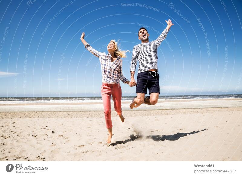 Glückliches, sorgenfreies Paar am Strand Beach Straende Strände Beaches Pärchen Paare Partnerschaft springen hüpfen Spaß Spass Späße spassig Spässe spaßig