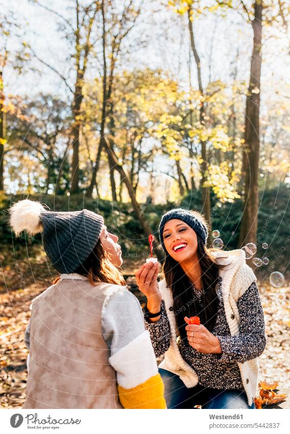 Zwei hübsche Frauen amüsieren sich mit Seifenblasen in einem herbstlichen Wald weiblich Freundinnen Herbst Spaß Spass Späße spassig Spässe spaßig schön Forst