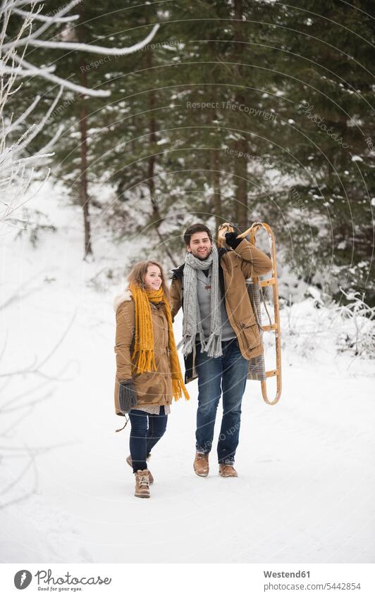 Glückliches junges Paar mit Schlitten im Winterwald Schnee Pärchen Paare Partnerschaft Wetter Mensch Menschen Leute People Personen glücklich glücklich sein