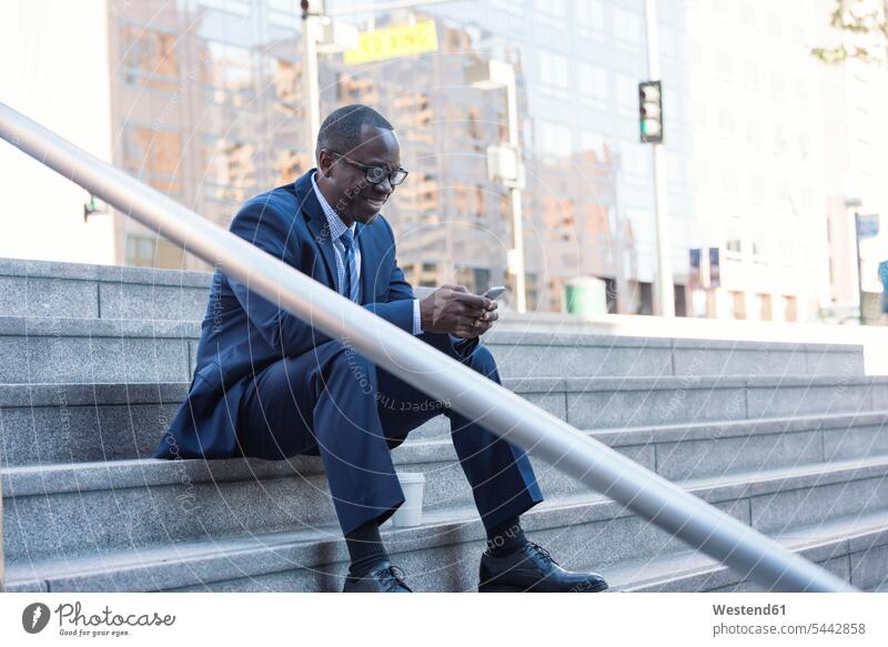 Lächelnder Geschäftsmann sitzt auf der Treppe und überprüft sein Handy Pause Mobiltelefon Handies Handys Mobiltelefone lächeln Businessmann Businessmänner
