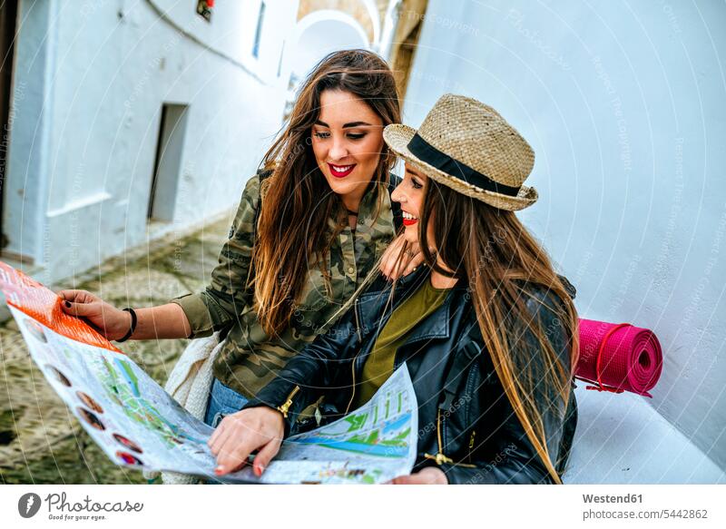 Zwei junge Frauen in einer Stadt, die auf eine Karte schauen lächeln Freundinnen Karten Freunde Freundschaft Kameradschaft staedtisch städtisch Touristin