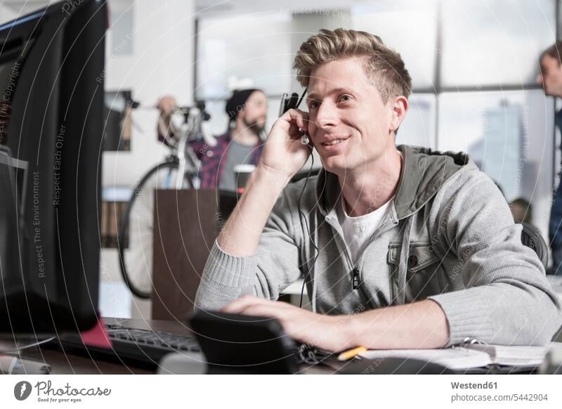 Junger Mann am Schreibtisch im Büro mit einem Headset Call Center Callcenters Call Centers Headsets Office Büros Männer männlich telefonieren anrufen Anruf