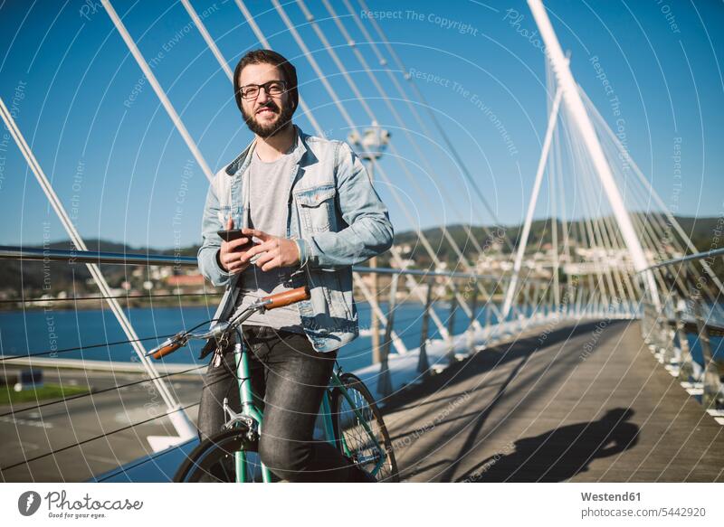 Lächelnder junger Mann mit Fixie-Rad auf einer Brücke Fahrrad Bikes Fahrräder Räder lächeln Männer männlich Raeder Verkehrswesen Transportwesen Erwachsener