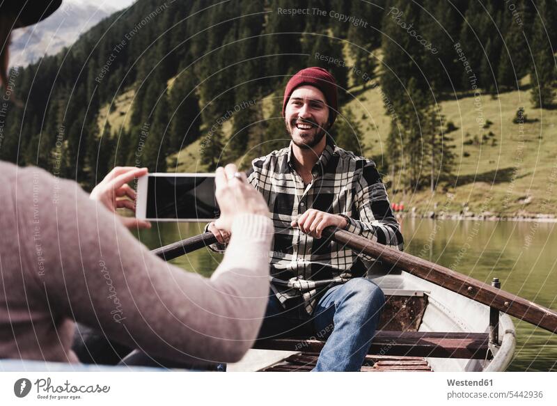 Österreich, Tirol, Alpen, Frau macht Handyfoto von lächelndem Mann im Ruderboot auf Bergsee See Seen Paar Pärchen Paare Partnerschaft Boot Boote fotografieren