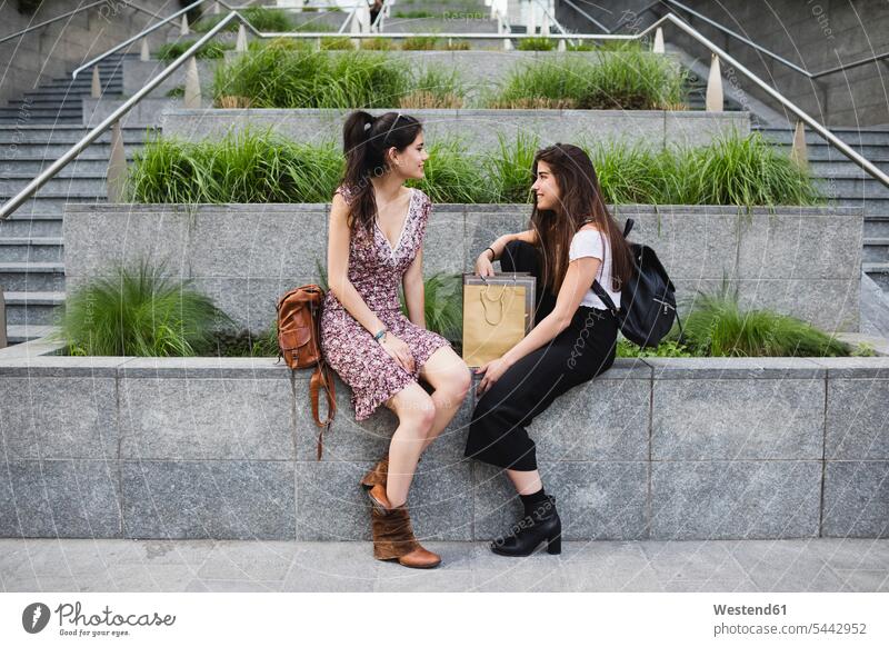 Zwei junge Frauen sitzen und unterhalten sich in der Stadt lächeln Freundinnen sprechen reden Freunde Freundschaft Kameradschaft weiblich Erwachsener erwachsen