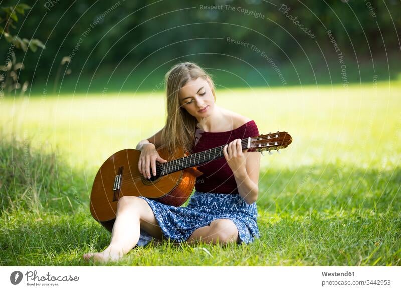Junge Frau sitzt auf der Wiese und spielt Gitarre Gras Gräser Graeser romantisch schwärmerisch schwaermerisch gefuehlvoll gefühlvoll Romantik üben ausüben Übung