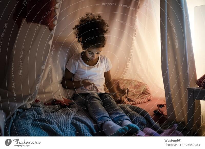 Kleines Mädchen sitzt im dunklen Kinderzimmer und schaut auf ein digitales Tablet lesen Lektüre sitzen sitzend spielen dunkel Zimmer Raum Räume Bett Betten