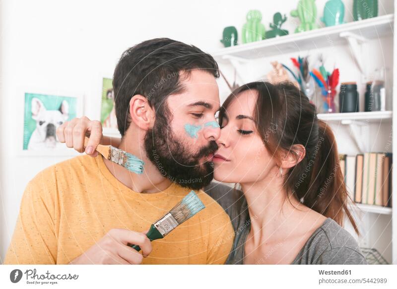 Junges Paar küsst sich und hält Pinsel Pärchen Paare Partnerschaft malen küssen Küsse Kuss Mensch Menschen Leute People Personen Innenaufnahme drinnen