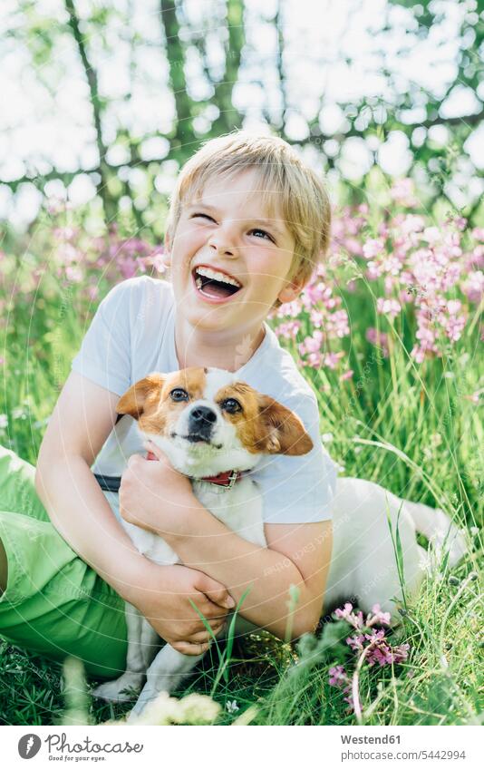 Porträt eines lachenden kleinen Jungen, der mit seinem Hund auf einer Wiese im Garten sitzt Hunde Portrait Porträts Portraits Buben Knabe Knaben männlich