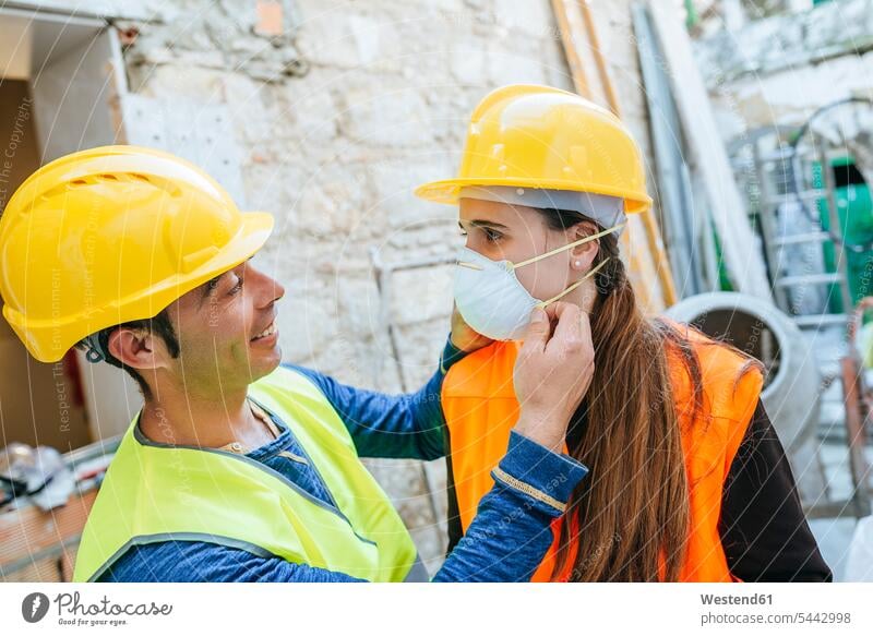 Mann hilft Frau beim Anlegen einer Staubmaske auf einer Baustelle aufsetzen arbeiten Arbeit Bauarbeiter Kollegen Arbeitskollegen Baustellen Handwerker