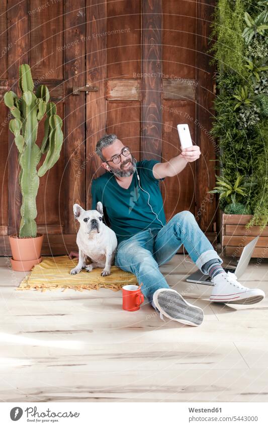 Bärtiger Mann sitzt mit seinem Hund zu Hause auf dem Boden und macht ein Selfie mit seinem Smartphone Hunde Männer männlich Selfies Haustier Haustiere Tier