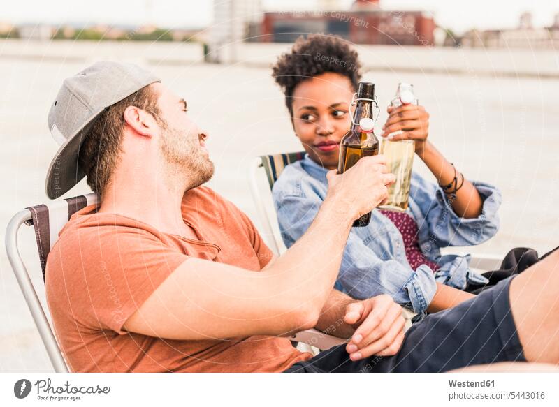 Junges Paar klimpert auf dem Dach mit Bierflaschen Party Parties Partys entspannt entspanntheit relaxt Pärchen Paare Partnerschaft trinken anstoßen zuprosten