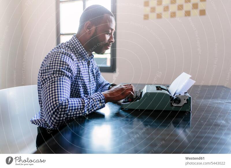 Junger Mann am Schreibtisch mit Schreibmaschine Schreibmaschinen Arbeitstisch Schreibtische Männer männlich Tisch Tische Erwachsener erwachsen Mensch Menschen