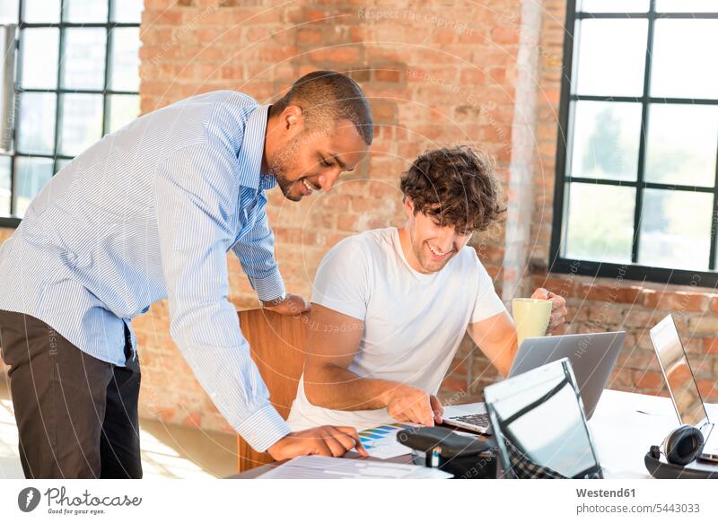 Zwei junge Geschäftsleute arbeiten in einem Arbeitsraum zusammen und benutzen Laptops Planung Pläne planen besprechen diskutieren Besprechung Coworking Space