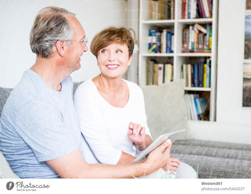 Älteres Ehepaar sitzt zu Hause auf der Couch und benutzt ein digitales Tablett Sofa Couches Liege Sofas sitzen sitzend lächeln Paar Pärchen Paare Partnerschaft