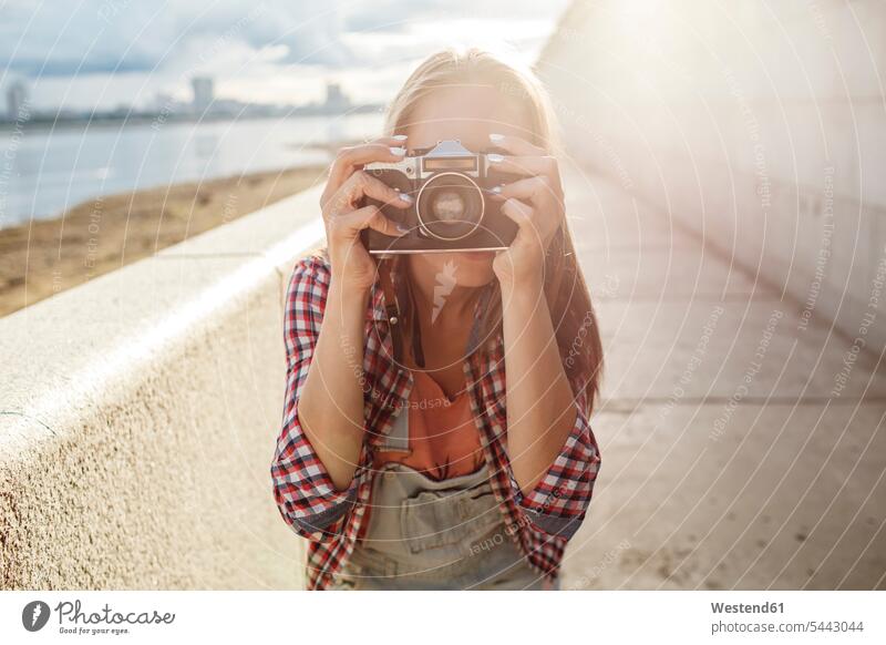Junge Frau beim Fotografieren mit einer Kamera am Flussufer weiblich Frauen Fotoapparat Fotokamera fotografieren Fluesse Fluß Flüsse Erwachsener erwachsen