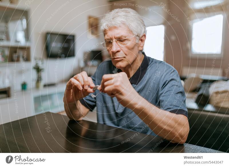 Älterer Mann untersucht Hörgerät Senior ältere Männer älterer Mann Senioren männlich Hörgeräte Hoergeraet Hoergeraete halten Erwachsener erwachsen Mensch