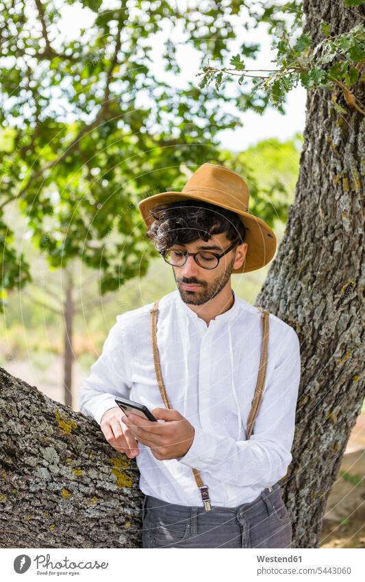 Mann trägt altmodische Kleidung und benutzt Mobiltelefon Männer männlich Handy Handies Handys Mobiltelefone Baum Bäume Baeume Erwachsener erwachsen Mensch