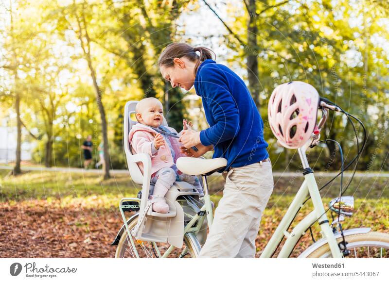 Mutter und Tochter fahren Fahrrad, das Baby trägt einen Helm und sitzt im Kindersitz Bikes Fahrräder Räder Rad lachen radfahren fahrradfahren radeln Fahrradhelm